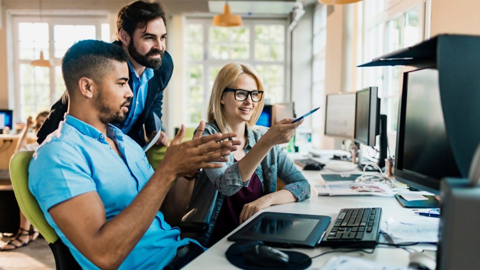Three employees in discussion and pointing to whats on the workstation screen