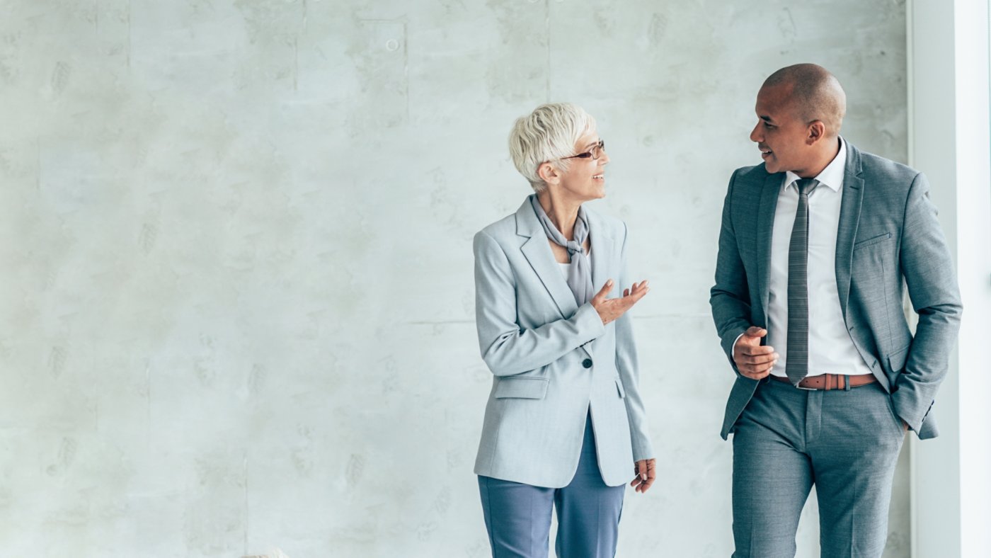 Two smiling business people walking through office hall and talking