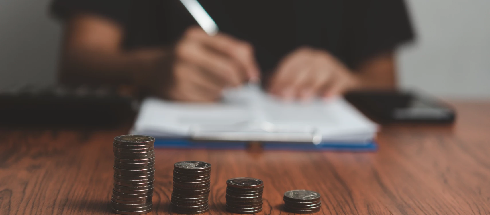 A pile of coin and an individual writing in a paper